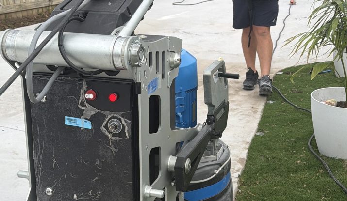 Floor grinder with dust-extraction hose beside a concrete slab